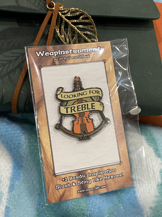 Crossbow violin enamel pin resting on blankets and notebooks