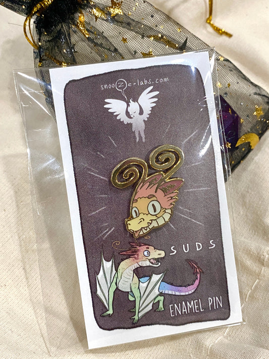 Dragon head enamel pin with her tongue sticking out resting on a see through bag and blanket