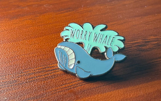 A worried whale enamel pin whose water spout says WORRY WHALE